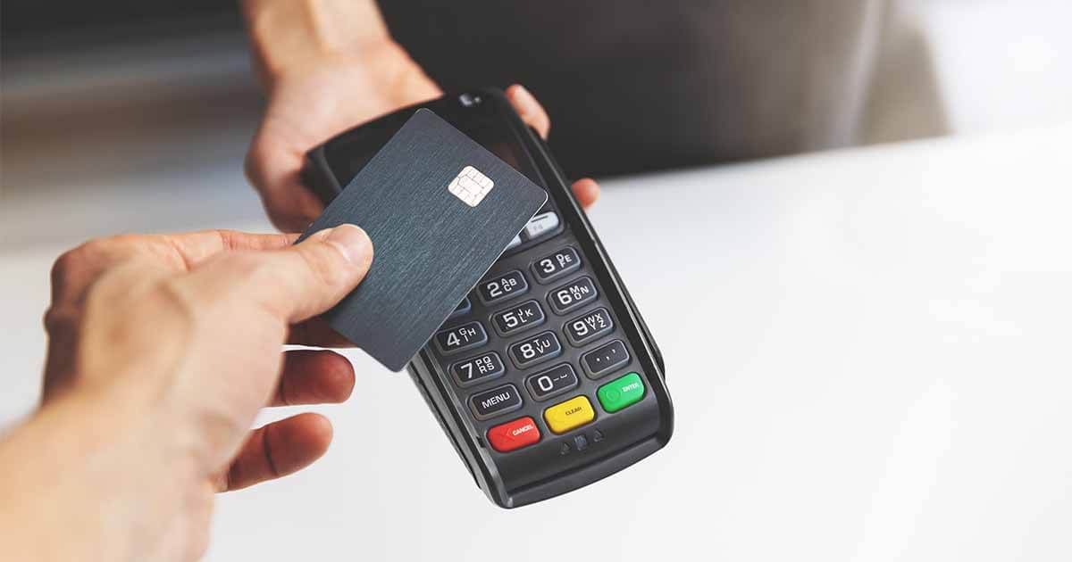 A person holds a credit card over a payment terminal to pay.