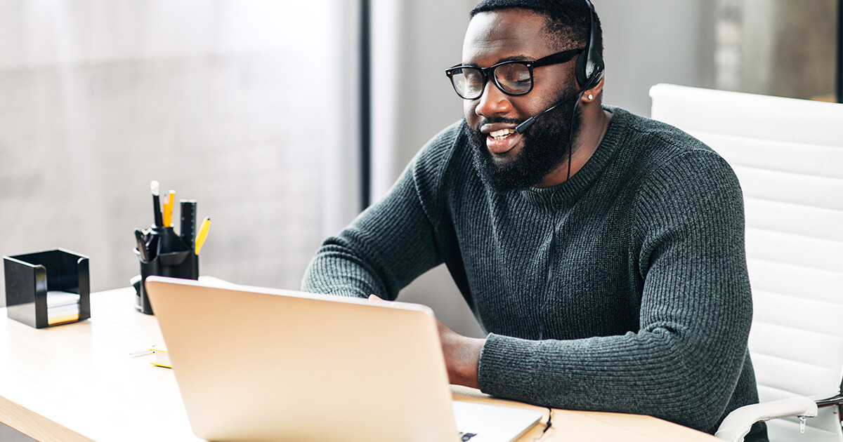 man sitting at desk working at laptop wearing phone headset