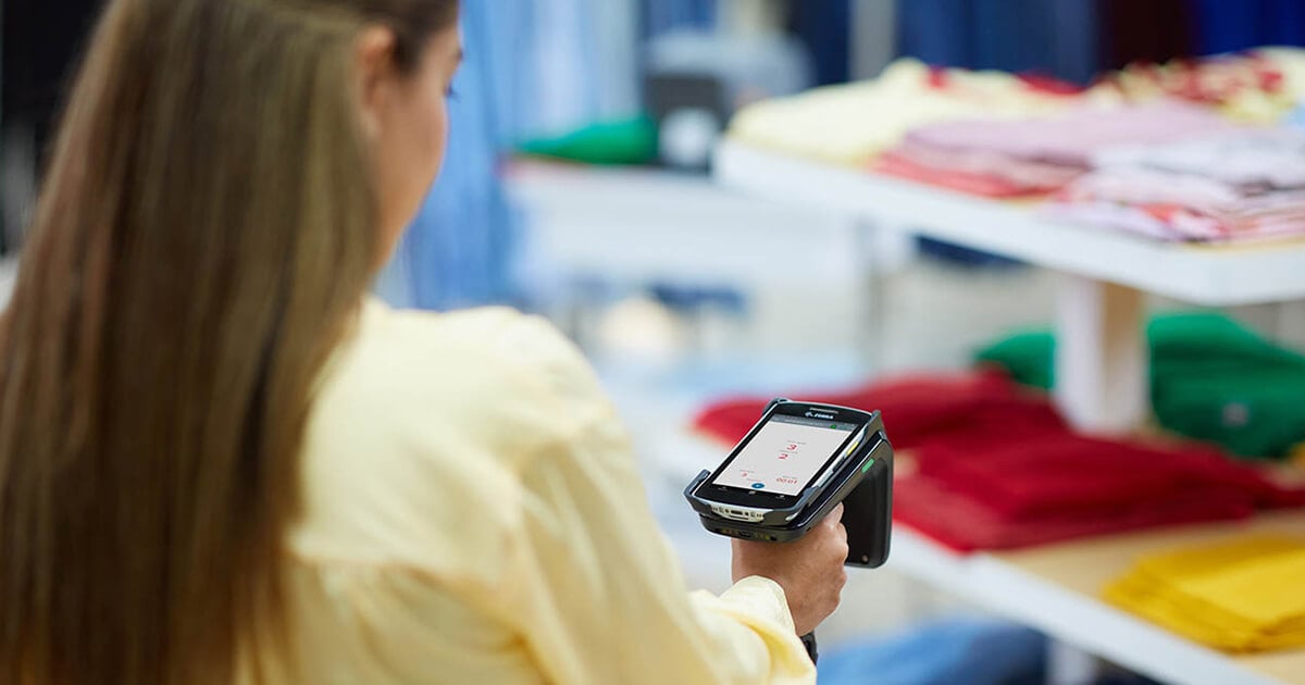 retail employee in yellow shirt holds RFID scanner pointed toward clothing shelves