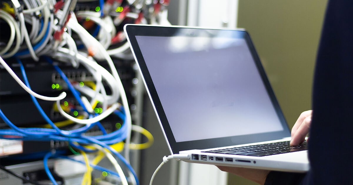 person holds laptop computer in network cabinet