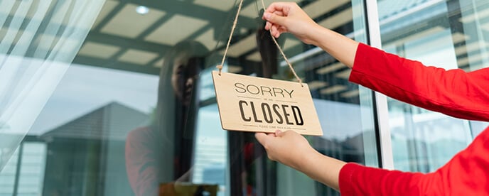 woman hanging store closed sign in ship window